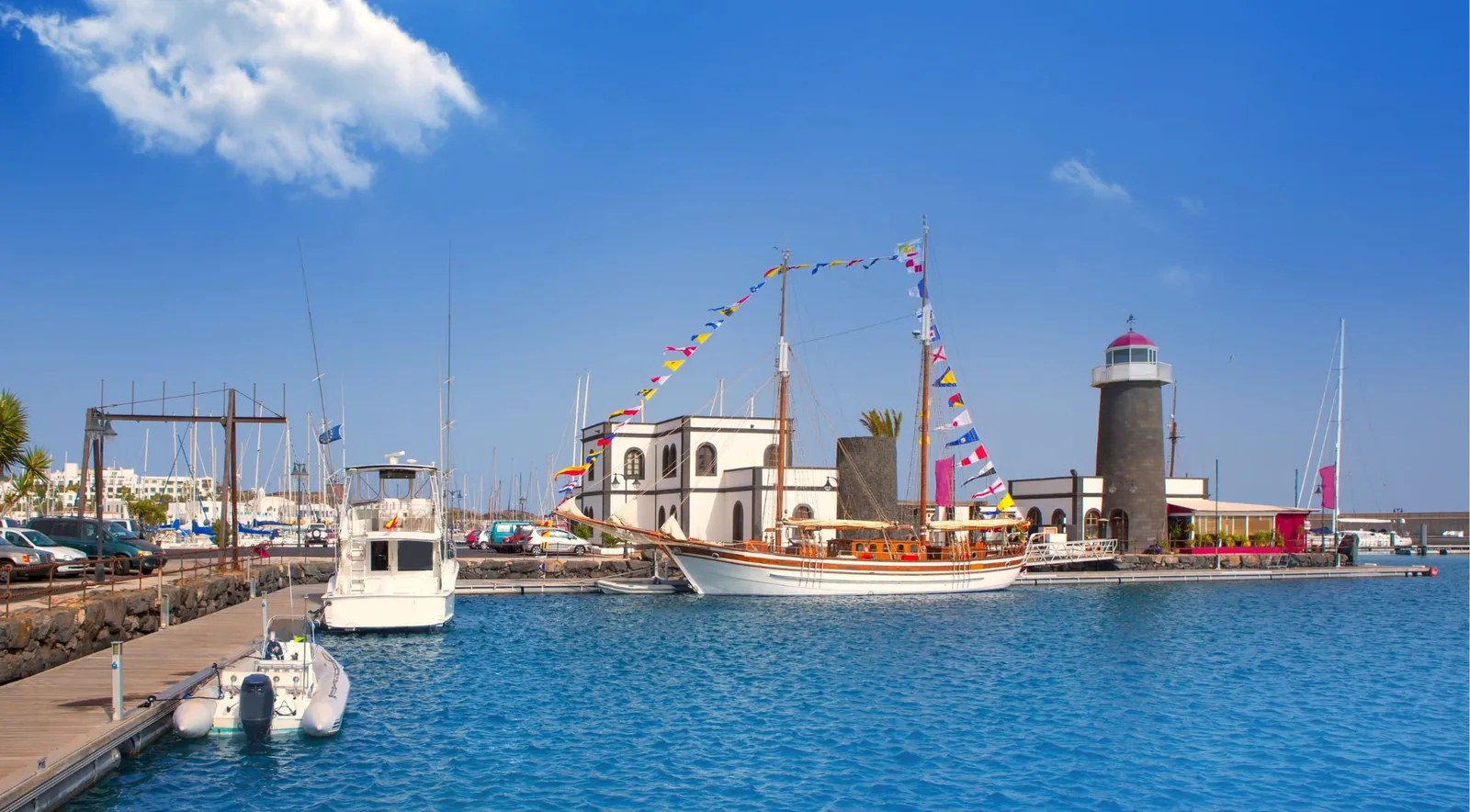 Marina Rubicón in Playa Blanca with a tall ship dressed in signal flags beside the stone lighthouse