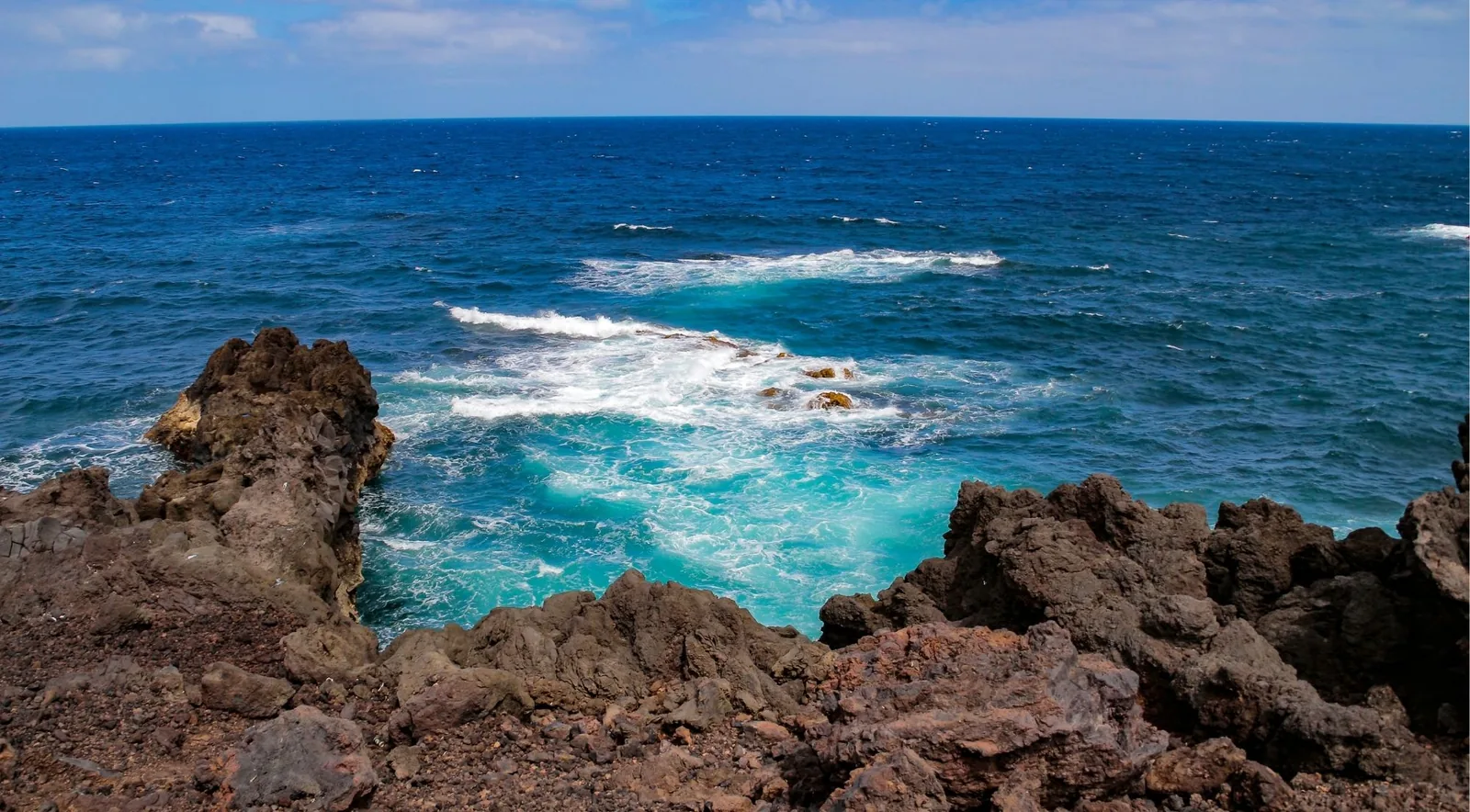 Jagged black lava rock dropping into turquoise surf on the south coast of Lanzarote