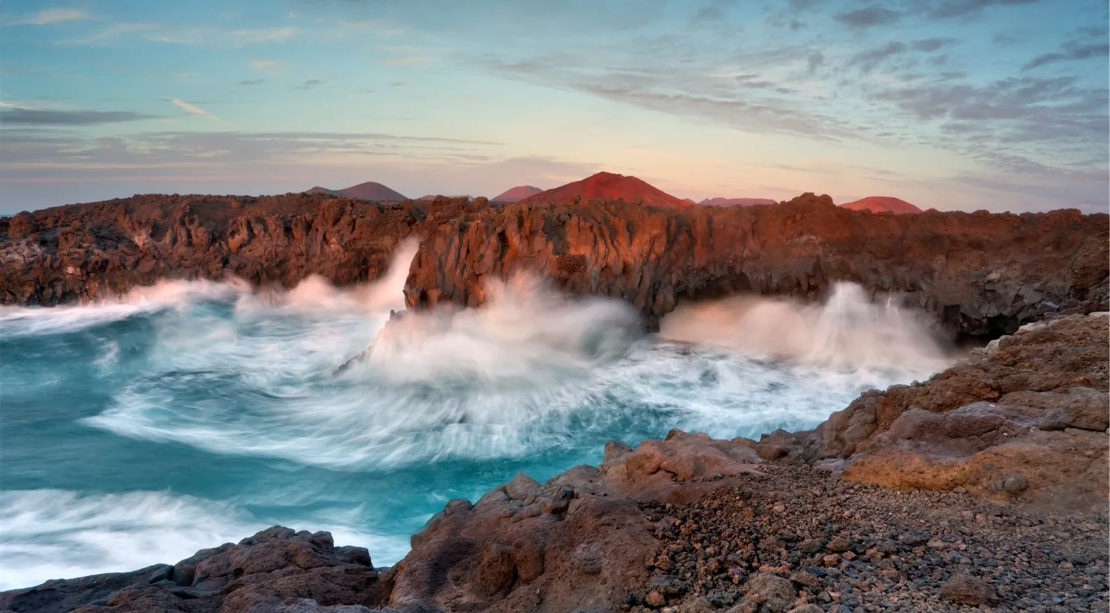 Atlantic swell exploding against the lava cliffs at Los Hervideros at sunset, volcanic cones on the skyline