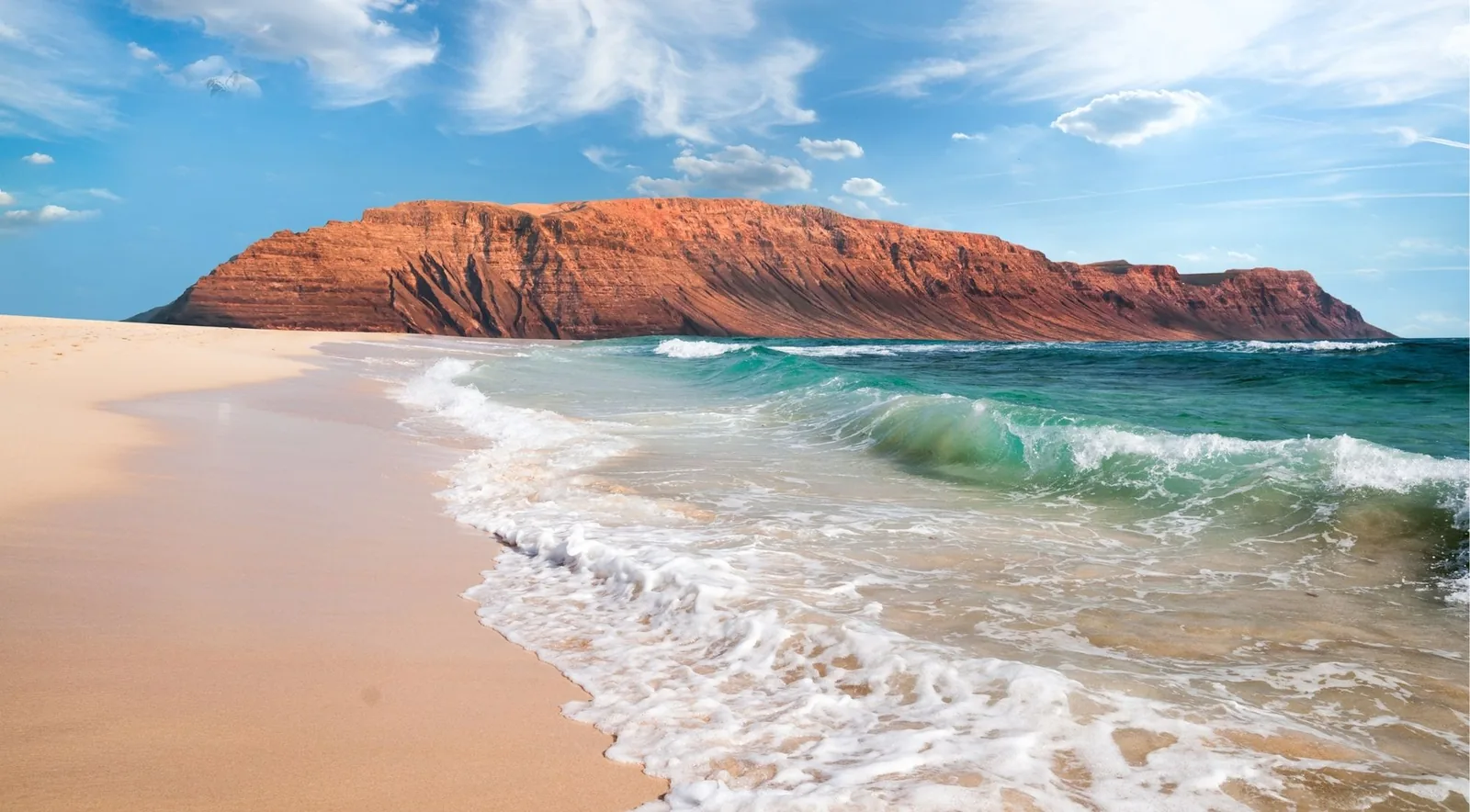White surf breaking on a golden beach below the red stratified cliffs of northern Lanzarote