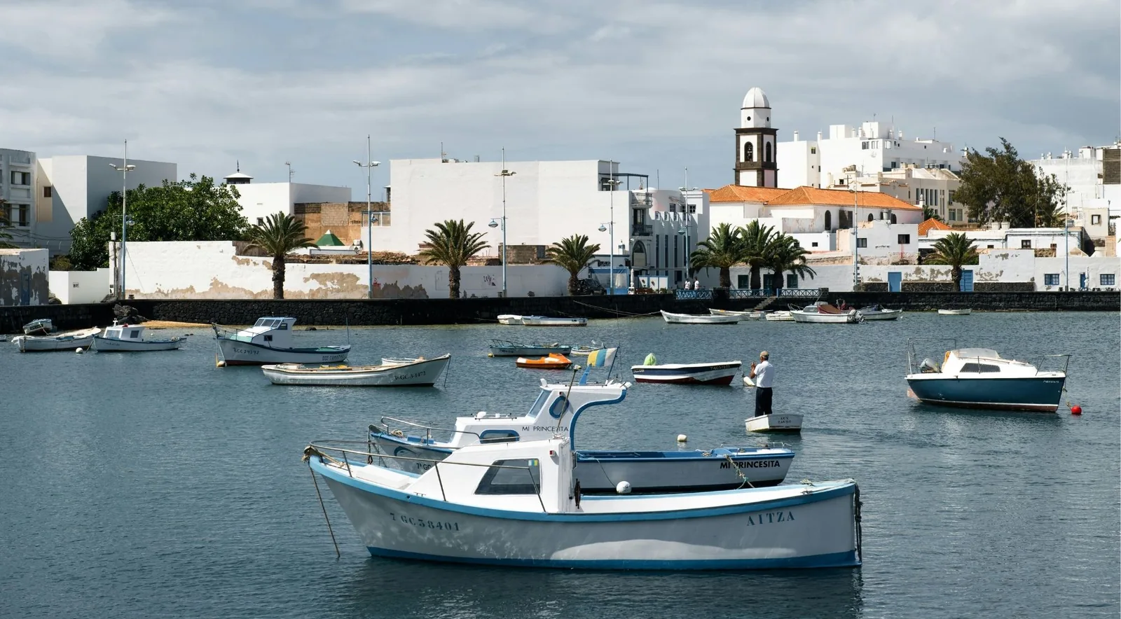 Small fishing boats moored in the Charco de San Ginés lagoon at Arrecife, with the white church tower behind
