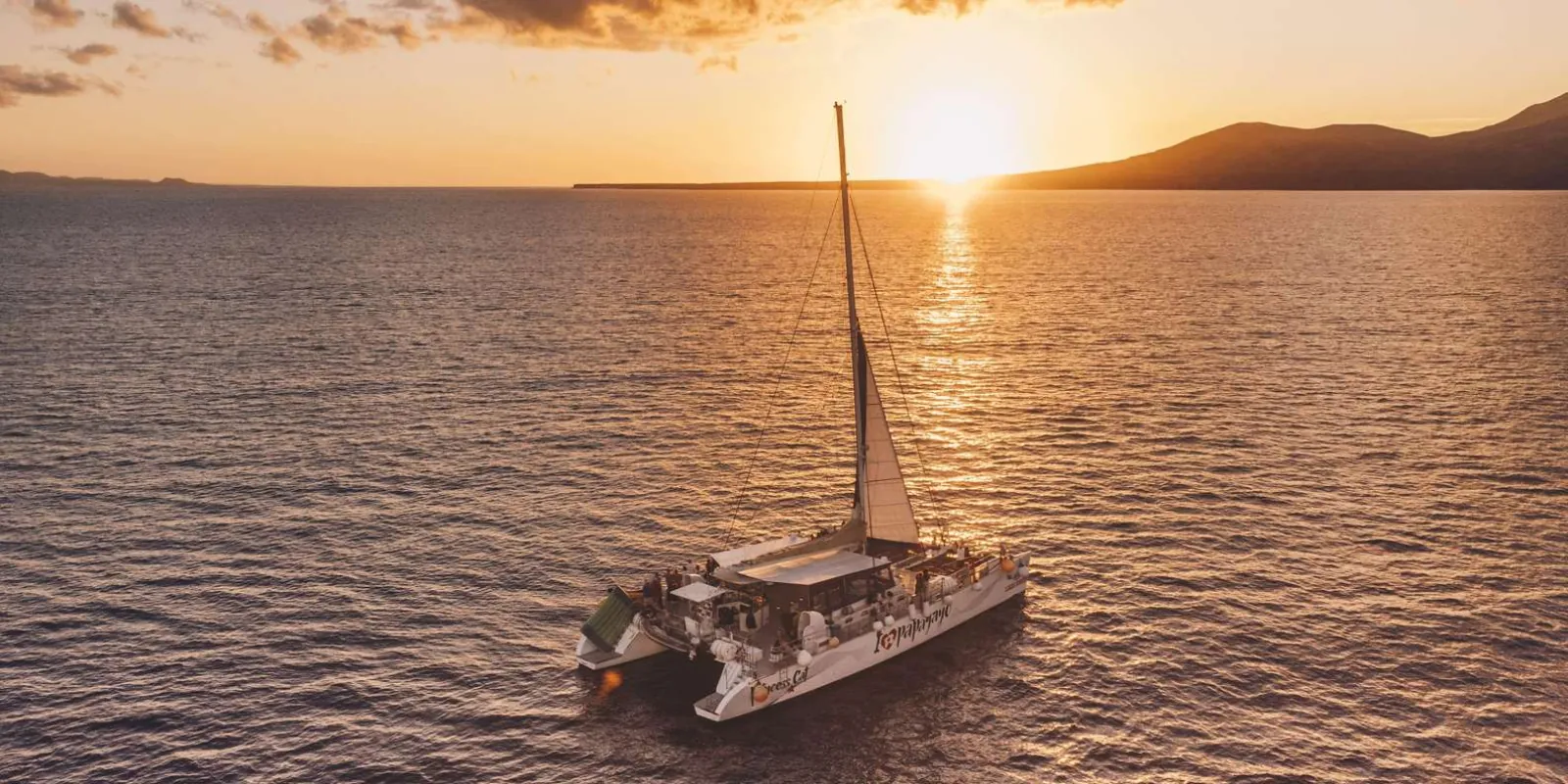 A Líneas Romero sailing catamaran at anchor on a golden Atlantic at sunset off Lanzarote