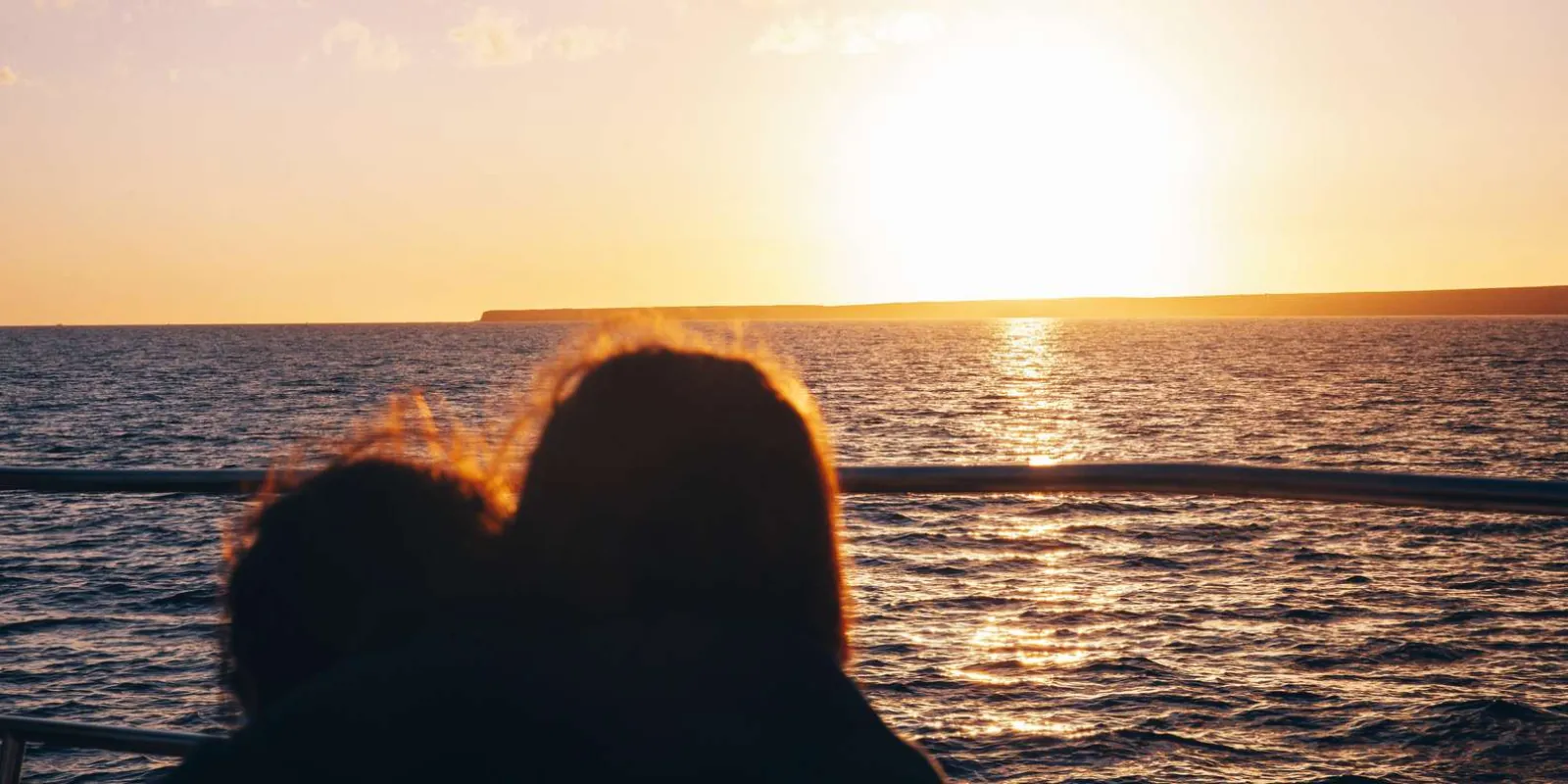 A couple silhouetted against the setting sun from the deck of the cruise