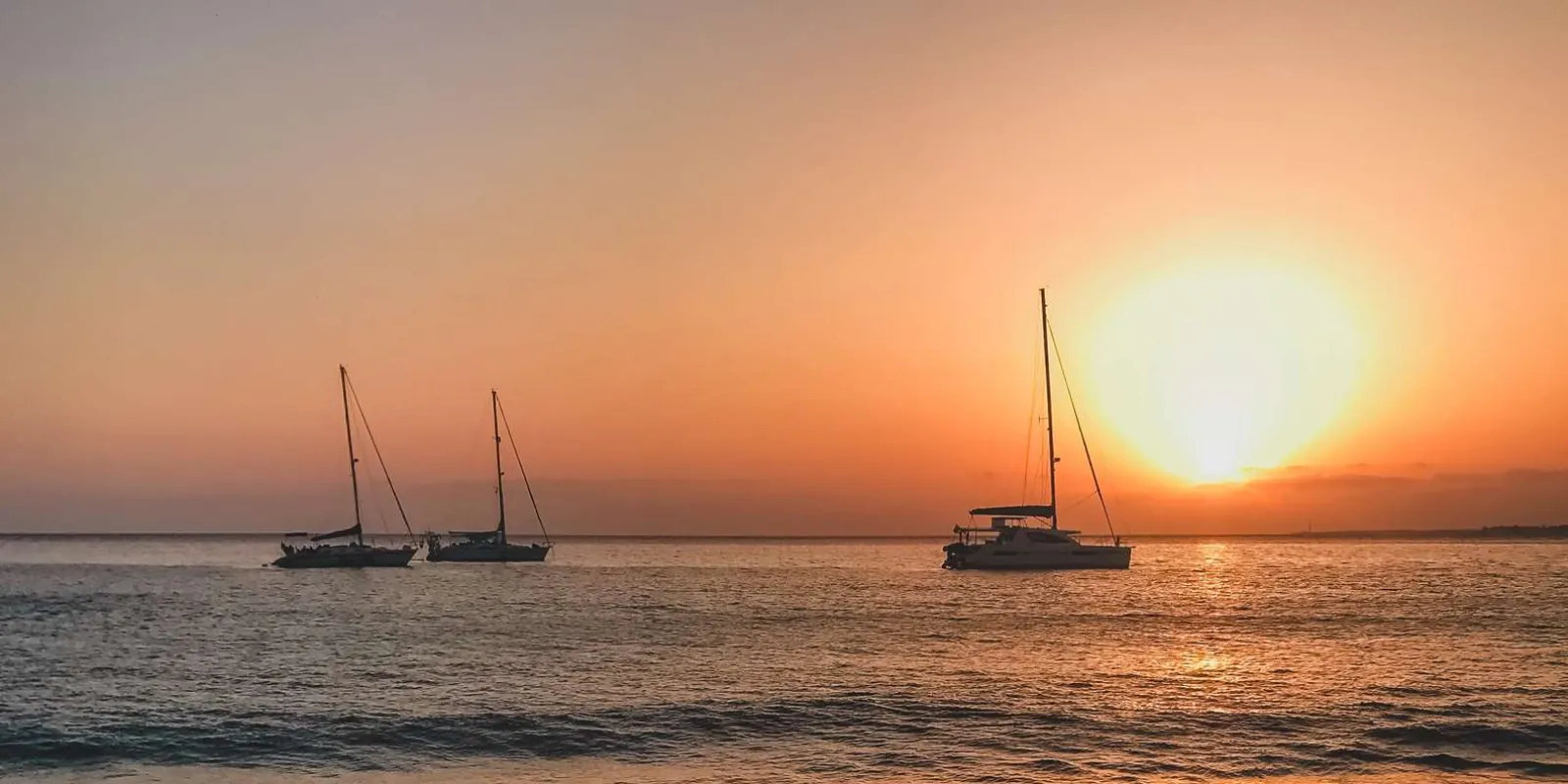 Three catamarans on a calm sea as the sun drops to the horizon off Lanzarote