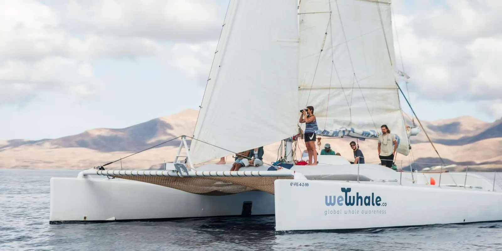 Guests on the deck of the white electric catamaran with its sail up