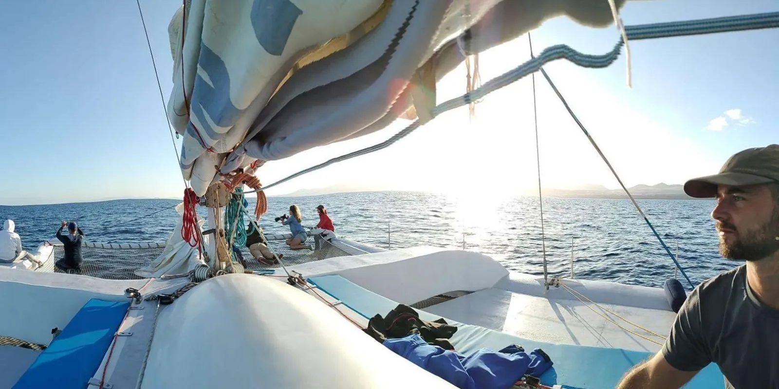 A crew member and passengers on the bow of the electric catamaran in low afternoon sun
