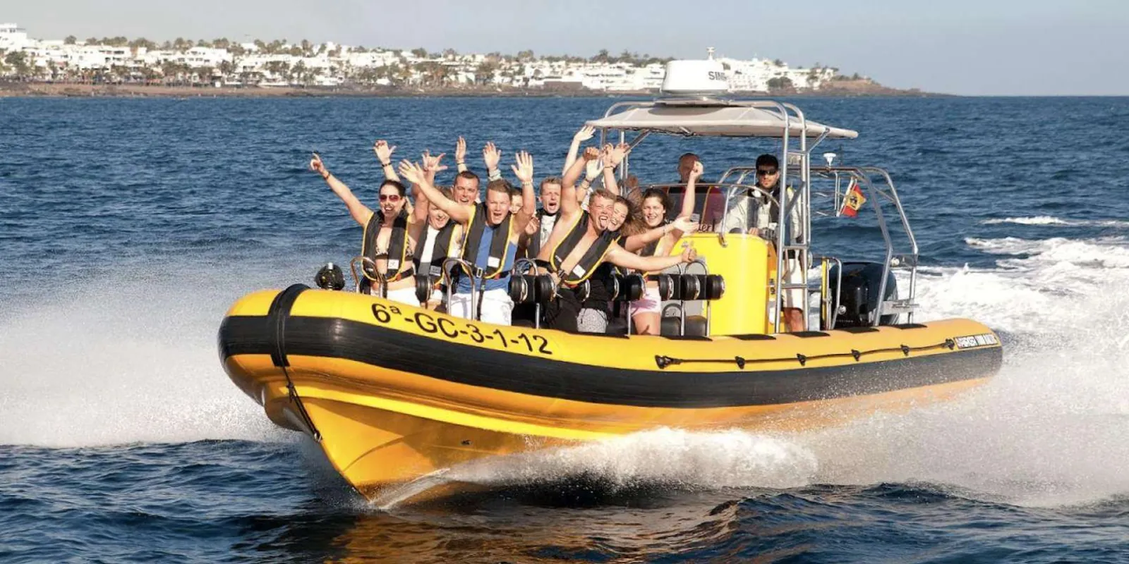 The yellow rigid inflatable at speed, throwing spray, passengers with arms raised