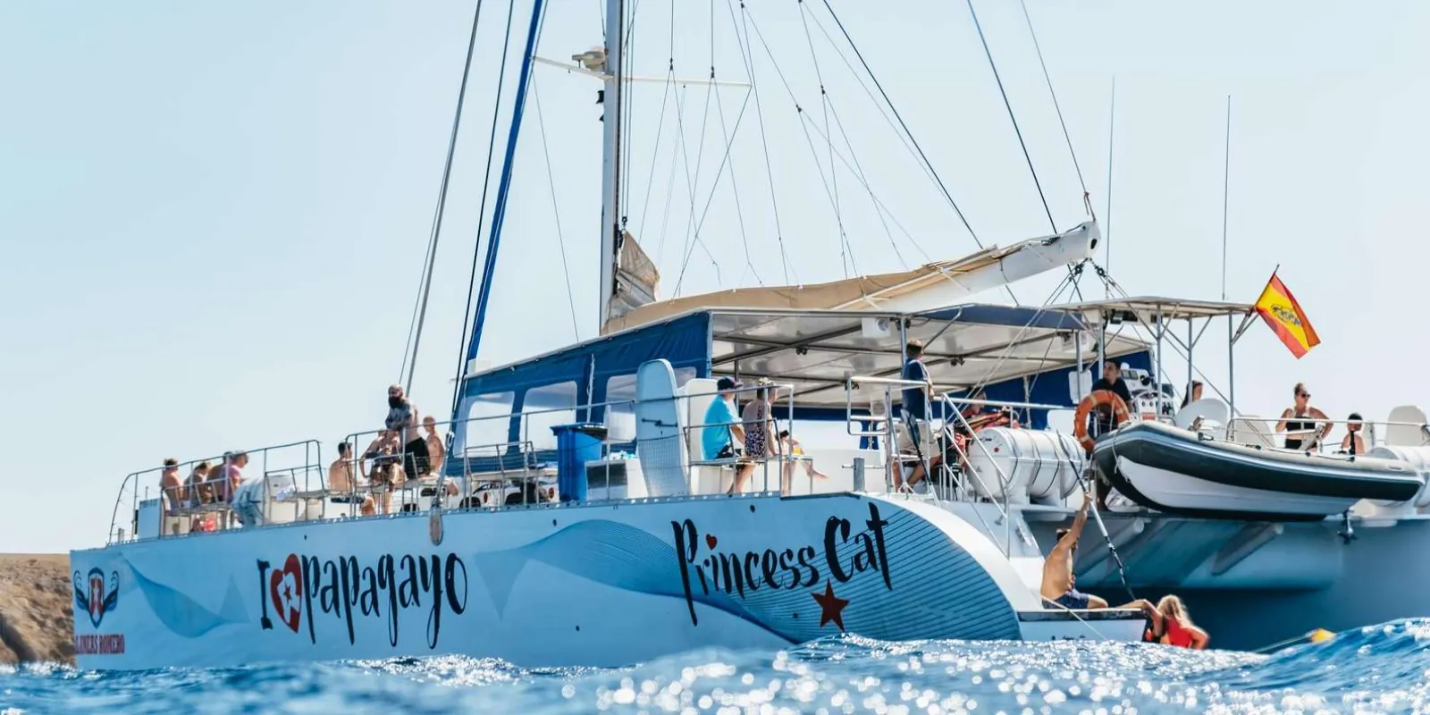 The blue Papagayo catamaran under way off Lanzarote with passengers lining the rail