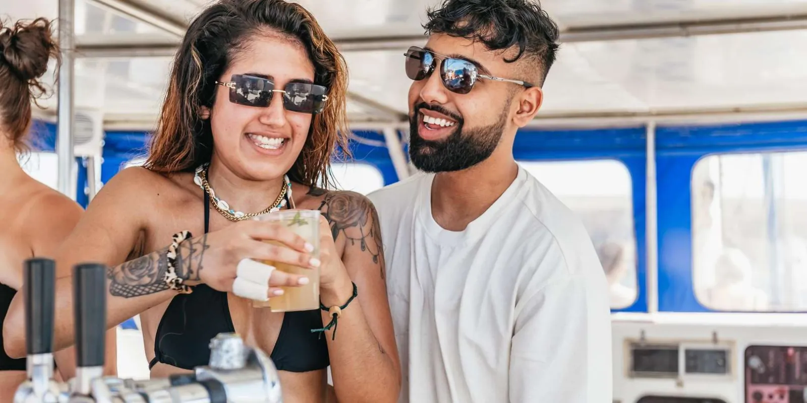 Two guests with drinks from the open bar in the shaded saloon of the catamaran